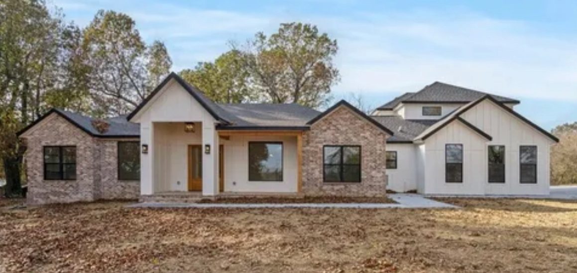 Modern two-story house with a mix of stone and white siding, surrounded by trees and grass.