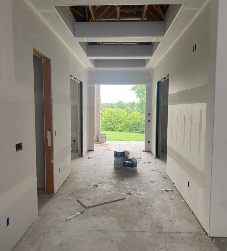 Interior hallway under construction with unfinished walls and a view of greenery outside.